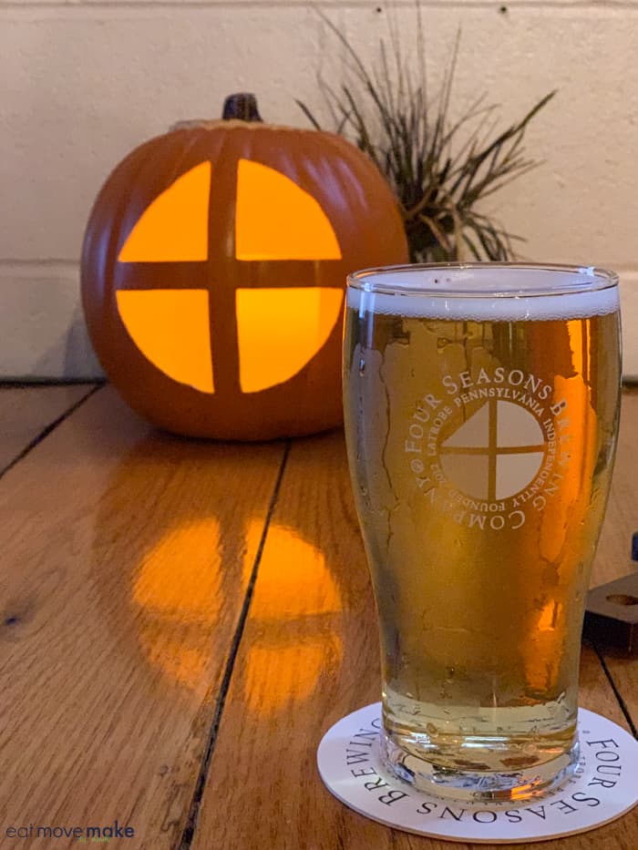 a glass of beer by a carved pumpkin