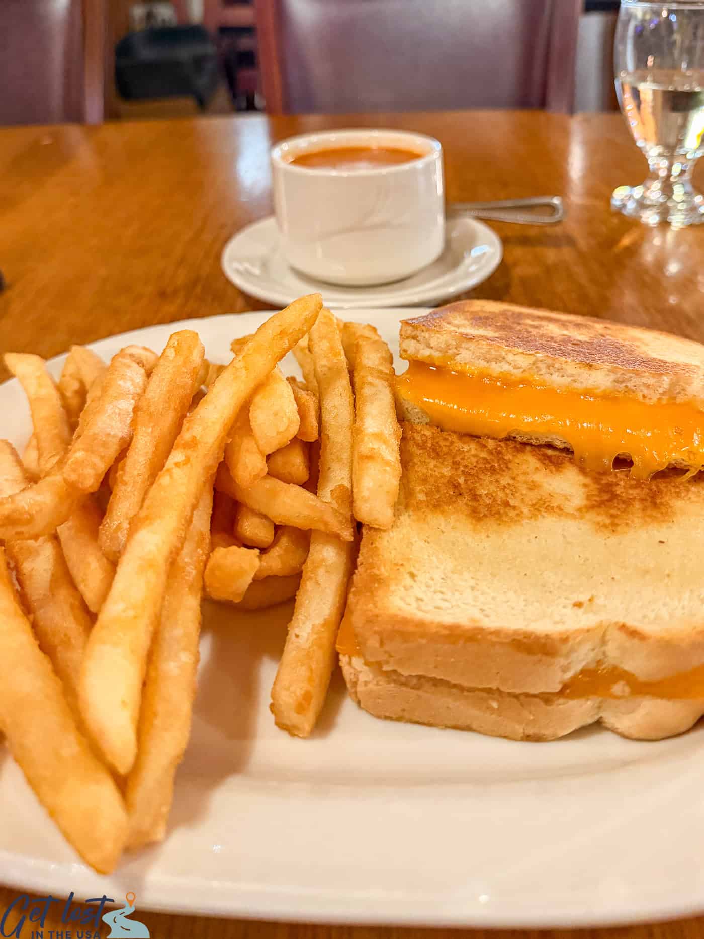 grilled cheese and fries on plate with tomato soup.