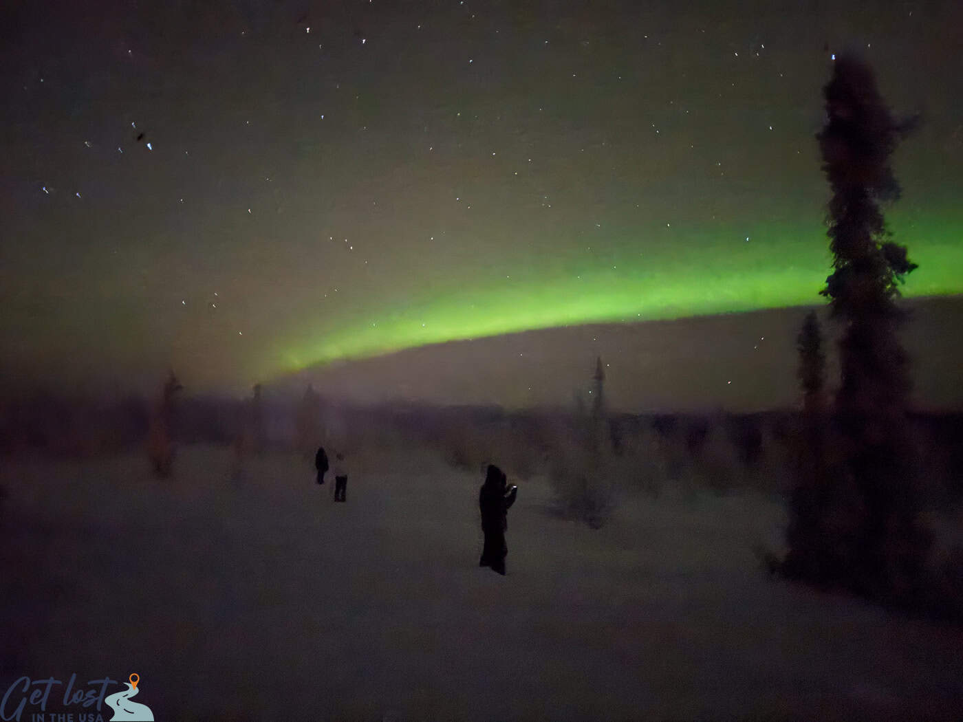 northern lights with people in foreground at Chena Hot Springs Resort Northern Lights Tour.